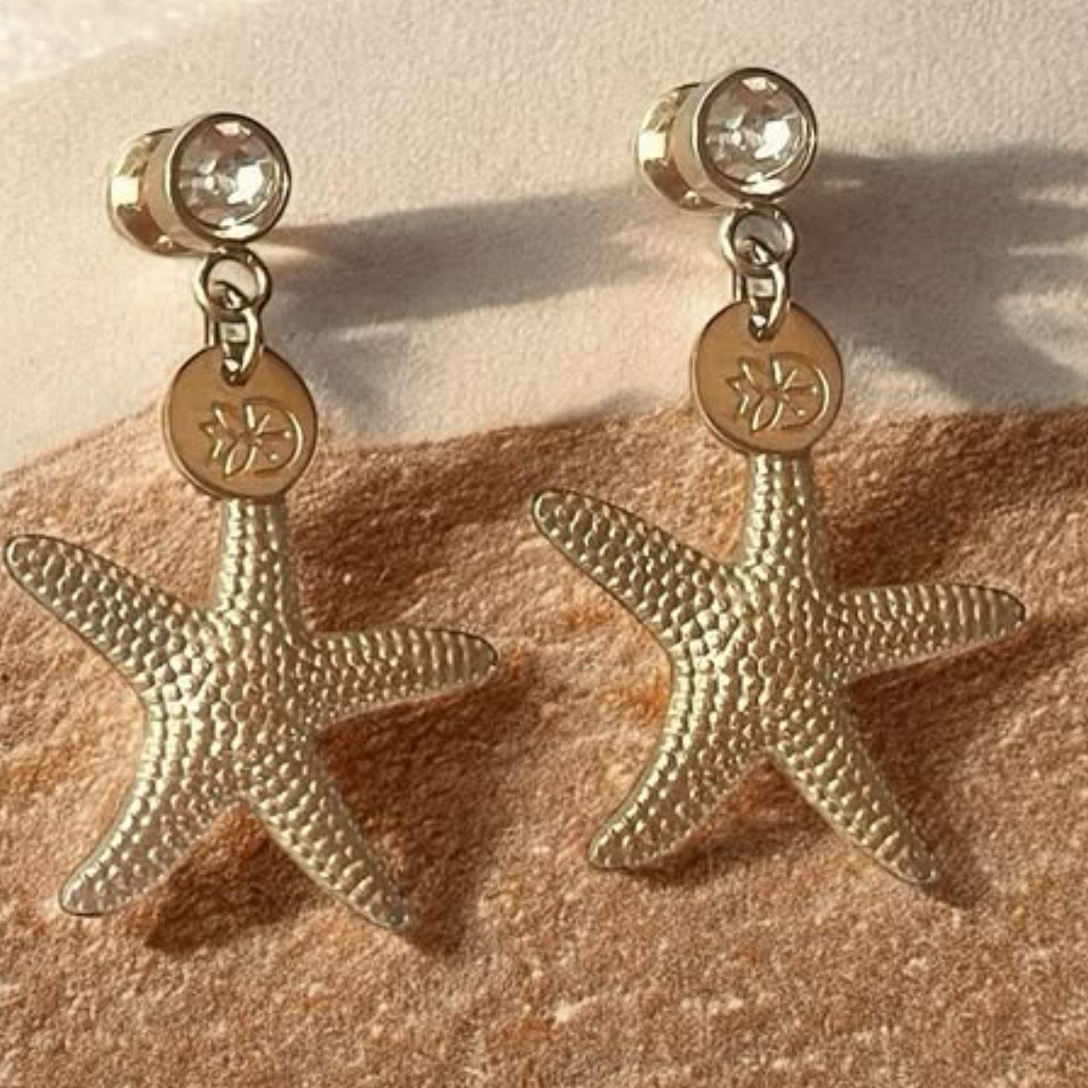 Gold starfish earrings with small stones on a beige surface